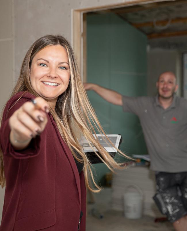 Zwei fröhliche Mitarbeiter, der Dienstleistungsfirma der ITB-Dresden GmbH, stimmen sich während des Sanierungsprozesses einer Wohnung ab. Die Mitarbeiterin aus der Verwaltung steht im Vordergrund und schaut in die Kamera.