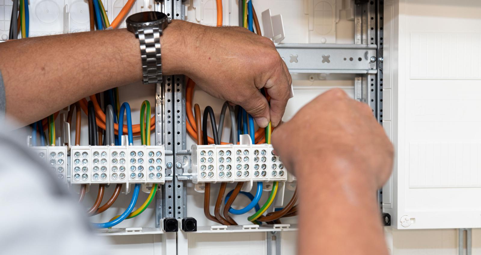 Bildausschnitt mit Händen eines Elektromeisters, beim anschließen von verschiedenen Kabeln im Zählerschrank.