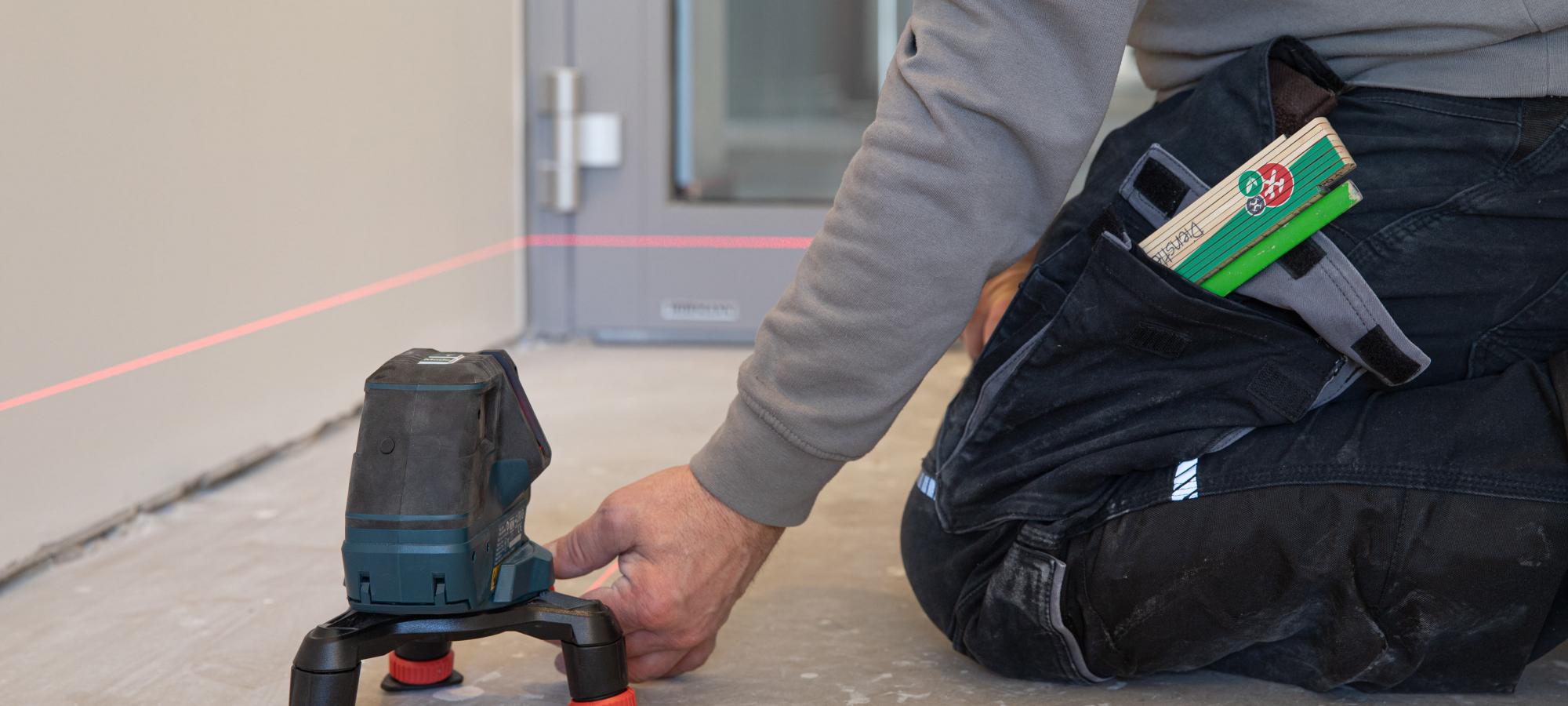 Bildausschnitt zeigt einen Fliesenleger der mittels Lasernivellierer den Boden für Bodenlegearbeiten vorbereitet