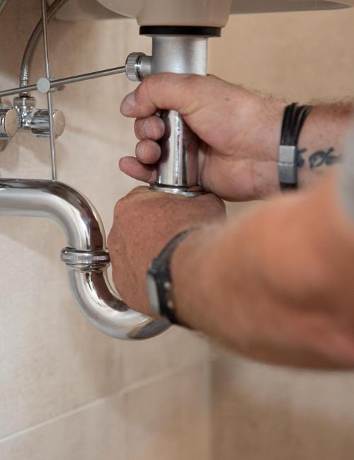 Bildausschnitt mit den Händen eines Hausmeisters beim Tauschen des Waschbecken-Siphons.