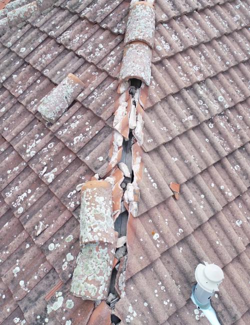 Ansicht von oben, mittels Drohneninspektionsflug. Zu sehen ist ein altes, stark beschädigtes Dach, mit zerbrochenen und teils mit flechten bewachsene Dachsteinen.