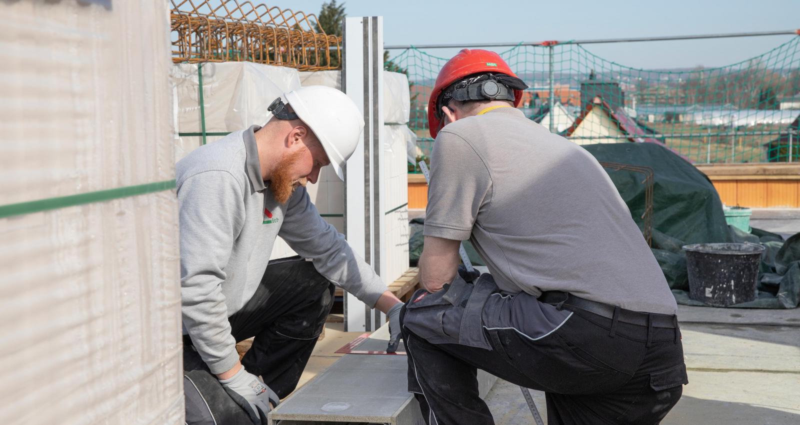 Zwei Bauhandwerker mit Bauhelmen im Rohbau eines Hauses, beim ausmessen der Schalung für einen Ringanker.