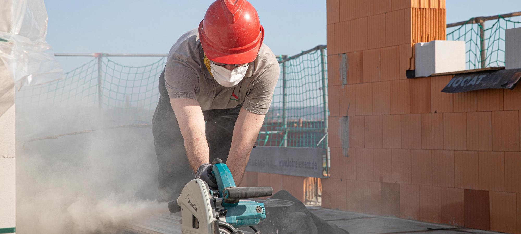 Ein ITB-Dresden GmbH Bauhandwerker mit rotem Bauhelm im Rohbau eines Hauses, säget die Schalung für einen Ringanker zu.