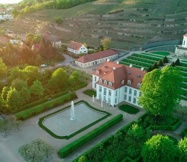 Drohnenflug in sommerlicher Abendstimmung über Schloss Wackerbarth in Radebeul, im Hintergrund die Weinhänge