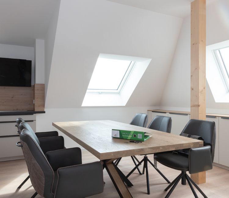 Blick in eine frisch eingerichtete, helle Wohnküche eines sanierten Wohnobjektes mit Fenstern, und Esstisch aus Holz.