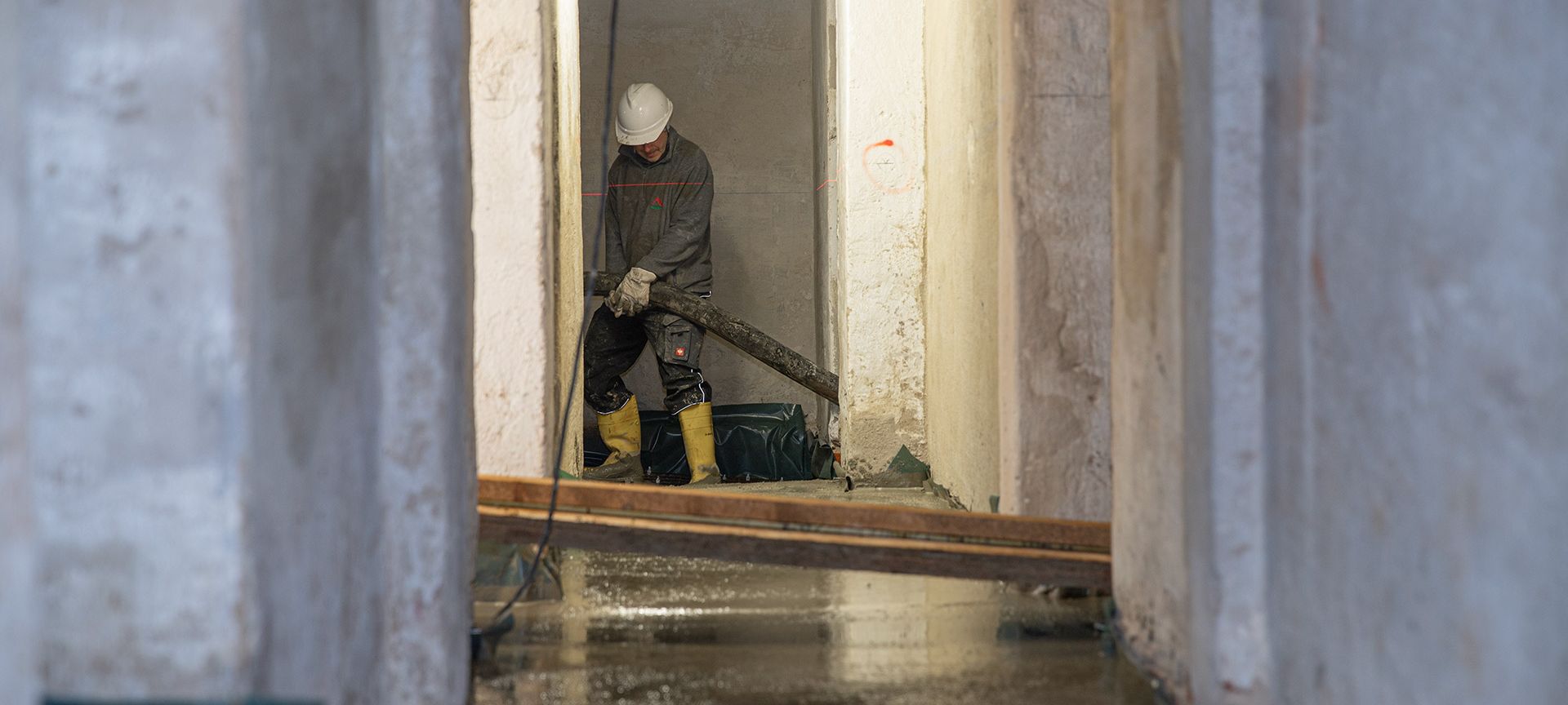 Bauhandwerker beim gießen von Fließestrich eines sanierten Kellergeschosses, mittels einer Estrichpumpe