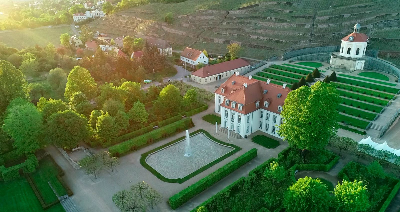 Drohnenflug in sommerlicher Abendstimmung über Schloss Wackerbarth in Radebeul, im Hintergrund die Weinhänge