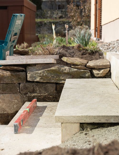 Garten und Landschaftsbauer beim Treppen- und Terrassenbau mittels heller Natursteinplatten
